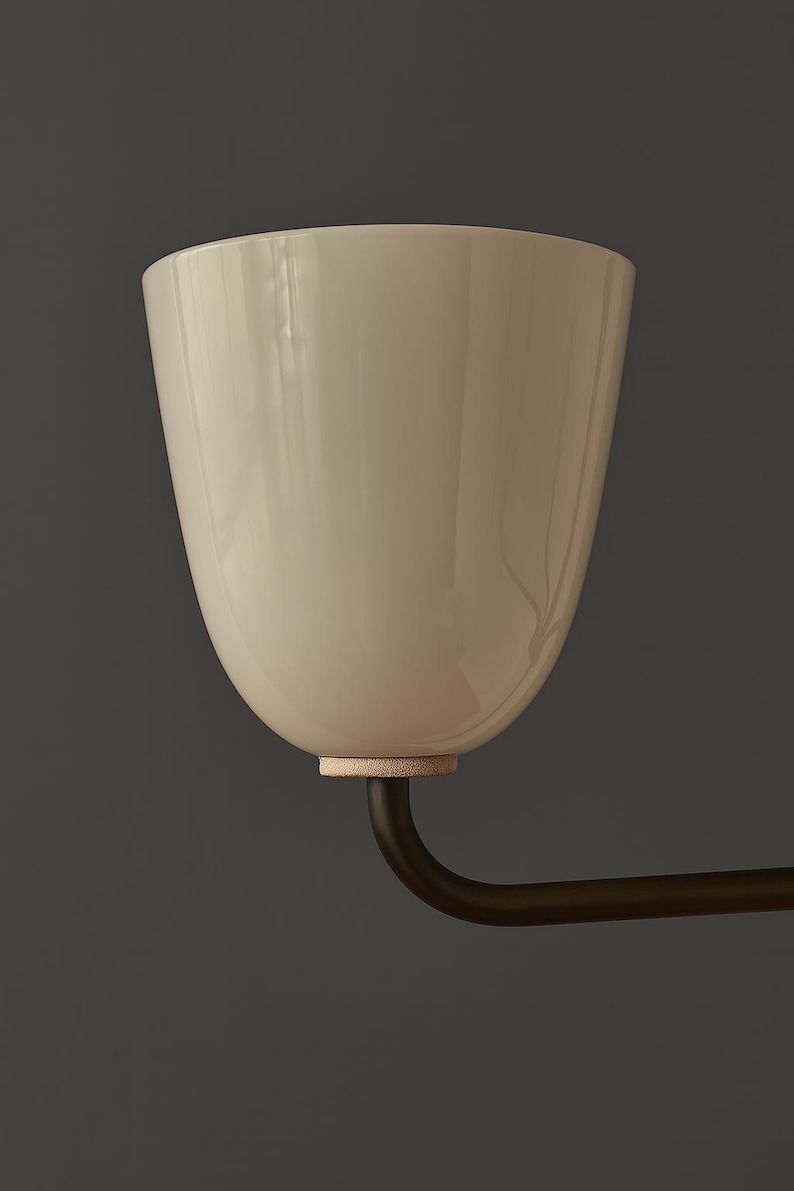 May include: A cream-colored, tulip-shaped light fixture with a dark bronze arm. The fixture has a smooth, glossy finish and a small, textured ring at the base. The background is a solid, dark gray.