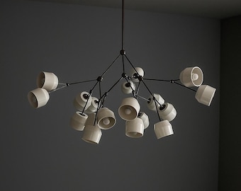May include: A modern chandelier with a black metal frame and multiple off-white ceramic shades. The light fixtures are arranged in a branching pattern, with each shade housing a light bulb. The fixture hangs from a chain.