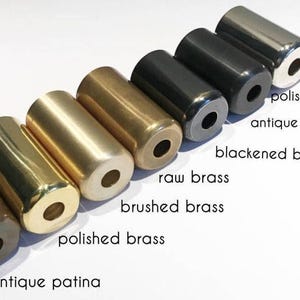 May include: An assortment of cylindrical metal objects in various finishes, including polished chrome, antique black, and polished brass. The text labels each finish, such as "blackened brass" and "antique patina". These objects are likely decorative hardware or components.