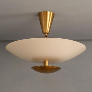 May include: A modern ceiling light fixture with a white, bowl-shaped shade and a gold-colored metal base and accents. The fixture is suspended from the ceiling by a gold-colored cone-shaped element.