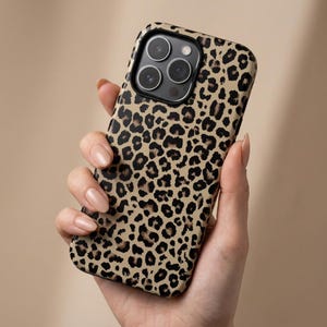 Puede incluir: Una funda de teléfono con estampado de leopardo marrón y negro. La funda tiene un acabado brillante y cubre la parte trasera y los laterales del teléfono. La funda tiene un recorte para la cámara.