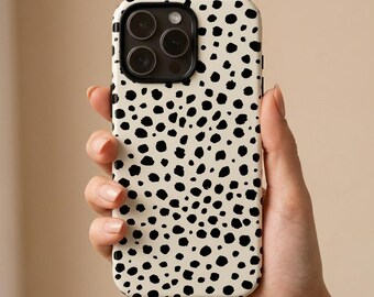May include: A smartphone case with a cream-colored background and a pattern of black spots. The case has a camera cutout and is held in a person's hand.