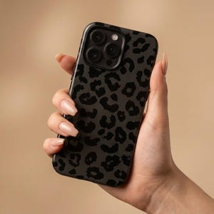 May include: A black phone case featuring a dark grey leopard print pattern. The case has a glossy finish and covers the back and sides of the phone. The phone case has a camera cutout and button covers.