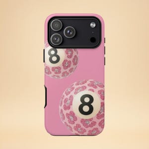 May include: Pink phone case featuring two stylized eight balls with a floral pattern. The number eight is in black on a white circle. The case has a black camera module.