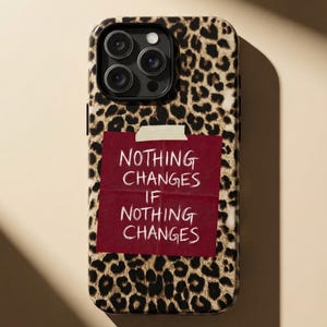 Pode incluir: Capa de telemóvel com padrão de leopardo e um post-it bordô que diz "NOTHING CHANGES IF NOTHING CHANGES" em texto branco. A capa tem um módulo de câmara com três lentes.