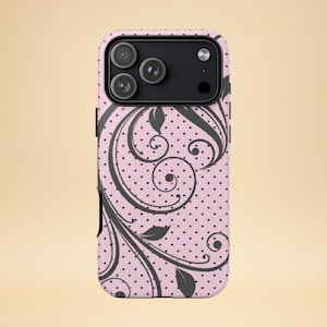 Könnte beinhalten: Eine rosa Handyhülle mit einem schwarzen Blumenmuster und einem Polka-Dot-Muster. Die Hülle hat ein schwarzes Kameramodul mit drei Objektiven. Das florale Design umfasst Wirbel und Blattformen.