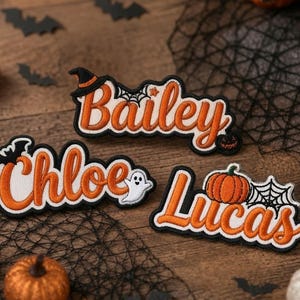 May include: Three embroidered patches featuring the names Bailey, Chloe, and Lucas in orange cursive script with black outlines. The patches include Halloween motifs such as a witch hat, a spider web, a ghost, and a small orange pumpkin.