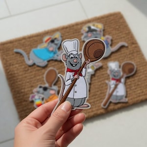 Può includere: Toppe ricamate raffiguranti chef di topi dei cartoni animati, con cappelli da chef e cucchiai di legno. Le toppe sono in varie pose e abiti, alcuni con occhiali da sole. Sono esposte su una superficie marrone.
