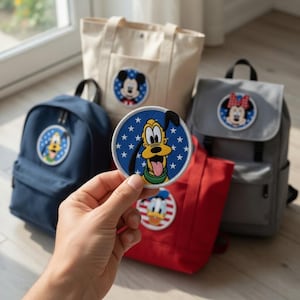 Puede incluir: Una colección de bolsos y mochilas con temática de Disney. Los bolsos son de varios colores, incluyendo azul marino, gris, rojo y beige. Cada bolso presenta un parche circular con un personaje diferente de Disney, como Mickey Mouse, Minnie Mouse, Pluto y Donald Duck.
