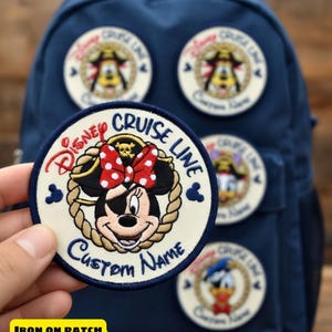 May include: A navy blue backpack with several Disney Cruise Line patches. One patch features Minnie Mouse in a pirate hat, with the text "Disney Cruise Line" and "Custom Name". Other patches feature Mickey Mouse and Donald Duck.