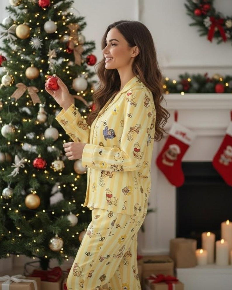 May include: Yellow pajama set with a Winnie the Pooh pattern. The set includes a button-down top and matching pants with vertical stripes. The background features a decorated Christmas tree and a fireplace with stockings.