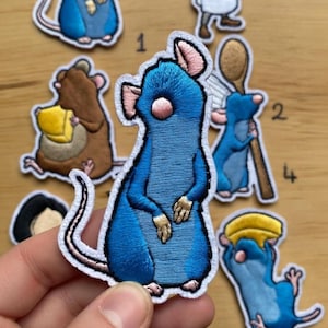 Può includere: Toppe ricamate raffiguranti topi dei cartoni animati in varie pose. Le toppe sono principalmente blu, marroni e bianche, con cuciture dettagliate. Un topo indossa un cappello da chef e un altro tiene un cucchiaio di legno. Le toppe hanno un bordo bianco.