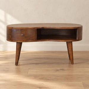 May include: A kidney-shaped coffee table crafted from dark brown wood. The table features a single drawer on the left side with a small, round metal knob and an open storage compartment on the right. It stands on four tapered wooden legs.