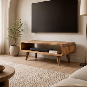May include: A low-profile, rectangular wooden media console featuring a smooth, light brown grain finish with rounded corners and an open storage shelf. The unit is supported by four tapered wooden legs and holds a black electronic device inside.