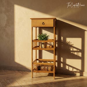 May include: A light brown wooden shelf unit with a drawer and multiple shelves. The unit has a small plant and a decorative pot on the shelves. The unit is placed against a beige wall and a wooden floor.