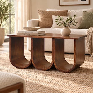 May include: A rectangular wooden coffee table featuring a smooth top surface and a base constructed from three continuous, U-shaped curved supports. The wood has a medium-brown finish with visible grain patterns throughout the entire structure.