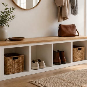 May include: A white storage bench with a natural wood top featuring four open cubby compartments. Two woven baskets are placed inside the outer cubbies, while a pair of light-coloured trainers and a pair of brown leather boots occupy the centre.