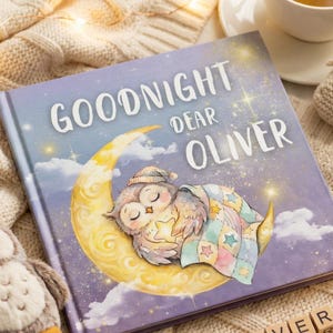 May include: A children's book titled "Goodnight Dear Oliver" with an illustration of a sleeping owl on a crescent moon. A plush owl toy, baby booties, and a cup of tea with chamomile flowers are also present. The scene is set on a cream-colored knitted blanket.