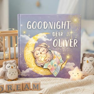 May include: A children's book titled "Goodnight Dear Oliver" with an illustration of a sleeping owl on a crescent moon. The image includes two plush owl toys, wooden blocks spelling "DREAM", and a star-shaped night light.