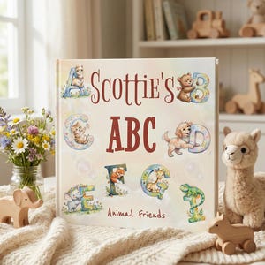 May include: A square children's book titled Scottie's ABC Animal Friends with a cream-colored cover featuring illustrated letters A through G decorated with animals like a llama, bear, kitten, puppy, fox, giraffe, and lizard in soft pastel colors.