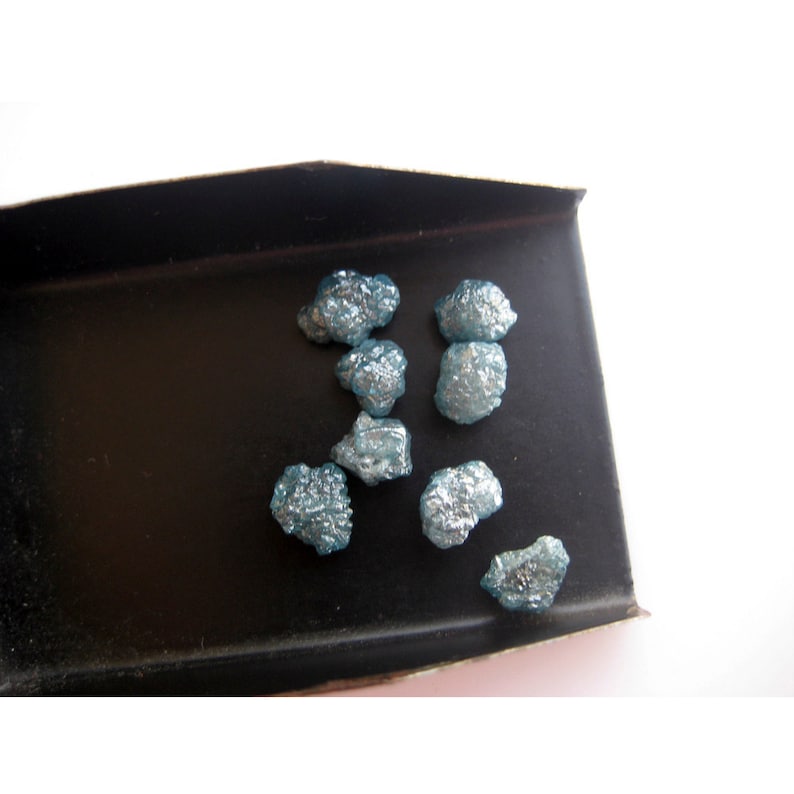 May include: A close-up of a tray containing several rough, blue-grey diamonds. The diamonds are scattered on a black surface.