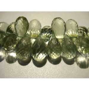 May include: A strand of faceted, light green gemstone beads. The beads are a mix of teardrop and oval shapes, strung together. The gemstones have a translucent quality, with visible internal facets. The overall color is a soft, pale green.