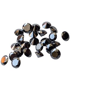 May include: A group of black round diamonds, also known as carbonado diamonds, are scattered on a white background.