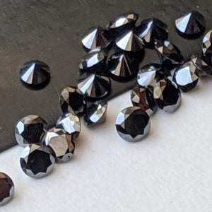 May include: A group of black round diamonds with a pointed top, scattered on a white surface. The diamonds are arranged in a random pattern, with some overlapping.