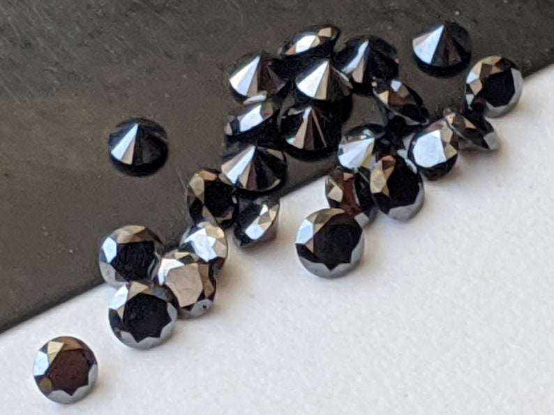 May include: A group of black round diamonds with a pointed top, scattered on a white surface. The diamonds are arranged in a random pattern, with some overlapping.