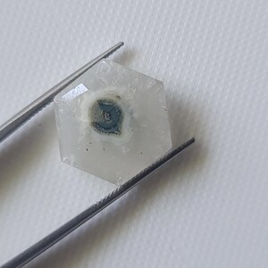 May include: A hexagonal clear quartz crystal with a dark gray and white inclusion in the center.