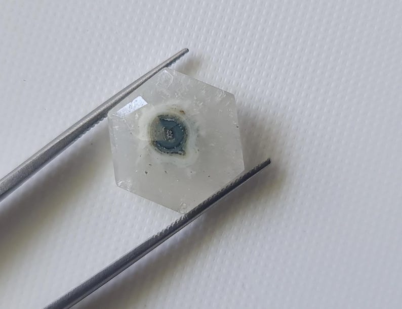 May include: A hexagonal clear quartz crystal with a dark gray and white inclusion in the center.