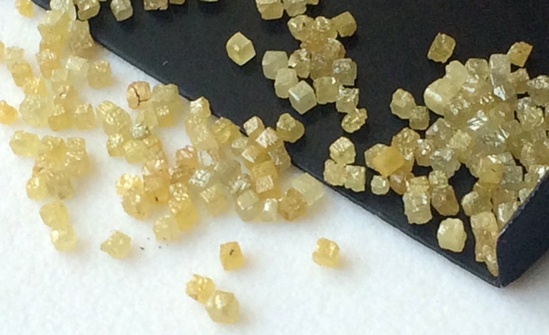 May include: A collection of small, yellow, faceted diamonds on a black surface. The diamonds are scattered and some are clustered together.