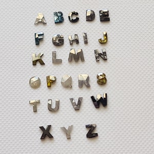 May include: A set of 26 diamond letters, each letter of the alphabet is represented by a single diamond. The diamonds are faceted and have a variety of colors, including clear, black, green, and yellow.