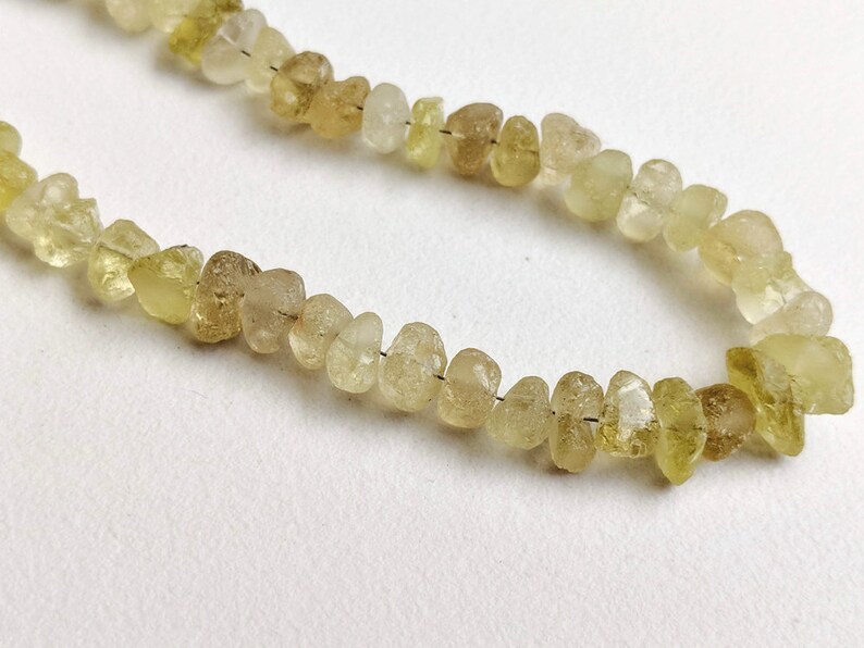 May include: A strand of light green and yellow gemstone beads. The beads are irregular in shape and have a rough, natural texture.