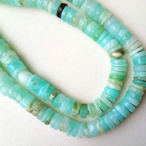 May include: A strand of light blue opal beads, with a variety of shapes and sizes. The beads are strung on a clear thread and are arranged in a double row.