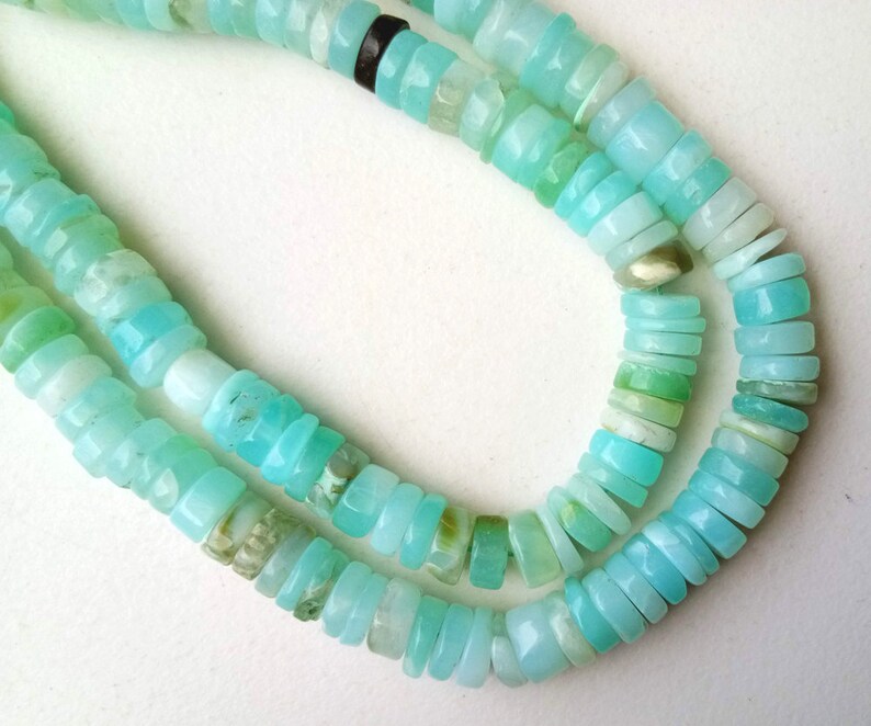 May include: A strand of light blue opal beads, with a variety of shapes and sizes. The beads are strung on a clear thread and are arranged in a double row.