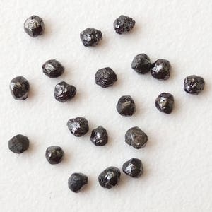 May include: A collection of black diamonds, also known as carbonado diamonds, in various sizes and shapes. These rough diamonds are unpolished and have a dark, opaque appearance.