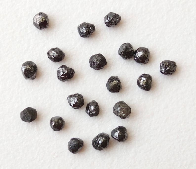 May include: A collection of black diamonds, also known as carbonado diamonds, in various sizes and shapes. These rough diamonds are unpolished and have a dark, opaque appearance.