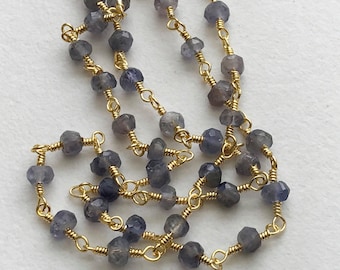 May include: A strand of faceted blue gemstone beads strung on a gold chain. The beads are approximately 4mm in diameter and have a wire wrapped around each bead.