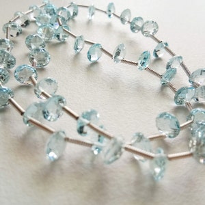 May include: A strand of light blue gemstone beads strung on a silver wire. The beads are faceted and have a round shape.