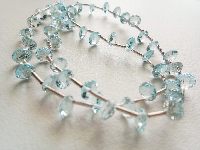 May include: A strand of light blue gemstone beads strung on a silver wire. The beads are faceted and have a round shape.