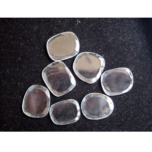 May include: Seven clear, faceted, glass stones in various sizes and shapes. The stones are arranged on a black surface.