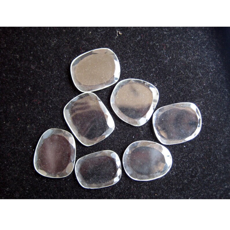 May include: Seven clear, faceted, glass stones in various sizes and shapes. The stones are arranged on a black surface.
