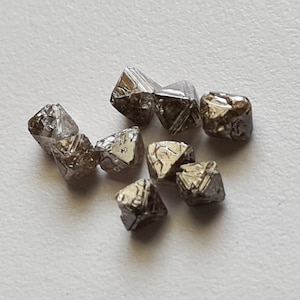 May include: A group of eight small, dark grey, octahedral diamonds. The diamonds are faceted and have a rough, natural appearance.
