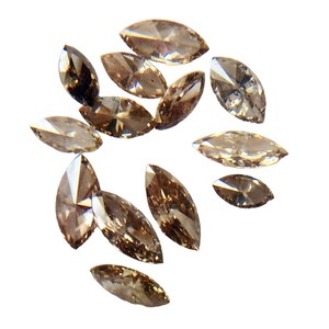 May include: A collection of brown marquise-shaped diamonds, scattered on a white background.