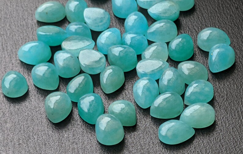 May include: A collection of loose, teardrop-shaped gemstones in a vibrant turquoise-blue color. Each stone features a smooth, polished, and rounded cabochon surface that reflects light, showcasing a translucent quality and consistent teal hue.