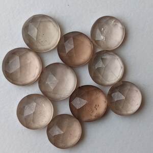 Puede incluir: Diez cabujones de piedra preciosa redondos, facetados y transl&uacute;cidos en tonos de marr&oacute;n claro y gris.