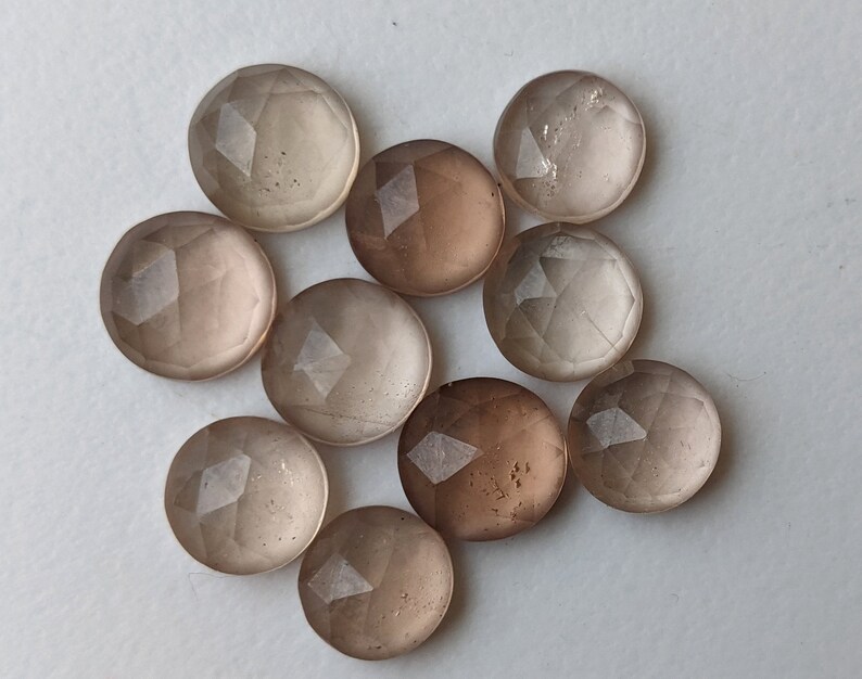 Puede incluir: Diez cabujones de piedra preciosa redondos, facetados y transl&uacute;cidos en tonos de marr&oacute;n claro y gris.