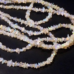 May include: A strand of white opal chip beads. The beads are irregular in shape and have a iridescent sheen.
