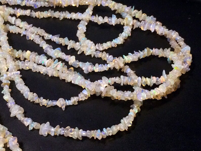 May include: A strand of white opal chip beads. The beads are irregular in shape and have a iridescent sheen.